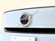 【ボルボの電気自動車を象徴するフロントフェイス】時代に合わせて変化するエンブレムデザイン。センターを斜めに大きく横切るラインと黒地に銀のアイアンマーク、これが最新ボルボのキャラクターアイコンです。